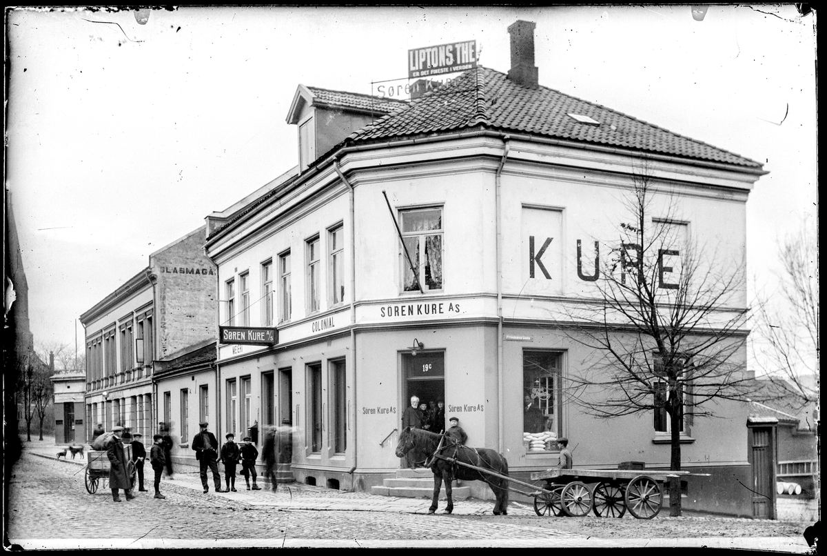 Dronningens gate 11, tidligere 19 på hjørnet av Prinsens gate i Moss. Kolonialforretningen til Søren Kure A/S,  Søren Kure var kjøpmann og ingeniør, og arbeidet som ingeniør i USA i tida 1900-1905.
Reklame på taket: Liptons THE er det fineste i verden.
Gateadresse Søren Kure A/S Dronningens gate 19  ifølge Adressebok for Fredrikshald, Fredrikstad, Moss, Sarpsborg 1911-12.
Moss Glasmagasin i bygningen til venstre, Dronningens gate 19.

Nils Johan Ringdal skriver i Moss bys historie: 
"Colonialkkjøbmand" Søren Kure solgte varer og melk fra melkespann, brakt inn fra gårdene omrkring. Hos ham var det alltid fullt av kunder. Når de kom fra herregårdene utenfor byen , ble de fulgt til døren med et kniks fra butikkdamen. Innimellom måtte førstedamen helt ut til landaueren for å ta i mot bestillingslisten."