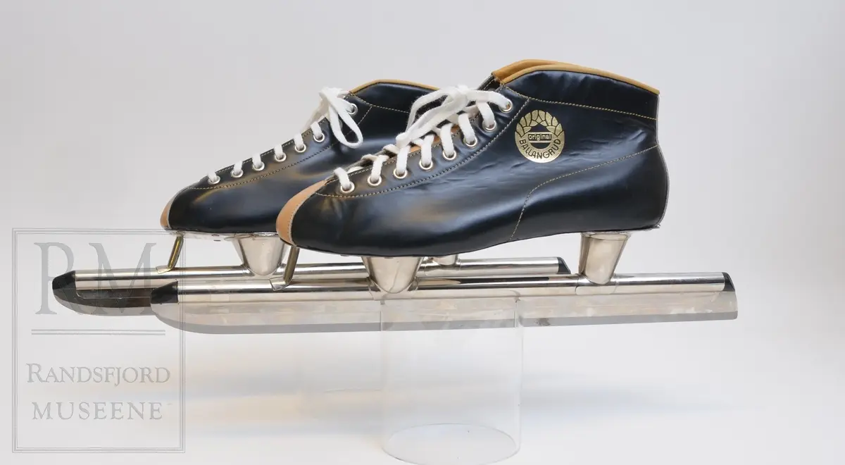 a-b) Skøyter: av svart skinn m / pløse og kant av beige skinn.Røret på skøytejernet avsluttet med plast i begge ender. 
c) plastpose til skøytene.
d) plaststykke.
e-f) Pappeske m/lokk. Brun papp med svart trykk på lokket.
g) pusseklut)
h) skøytefett i tube.