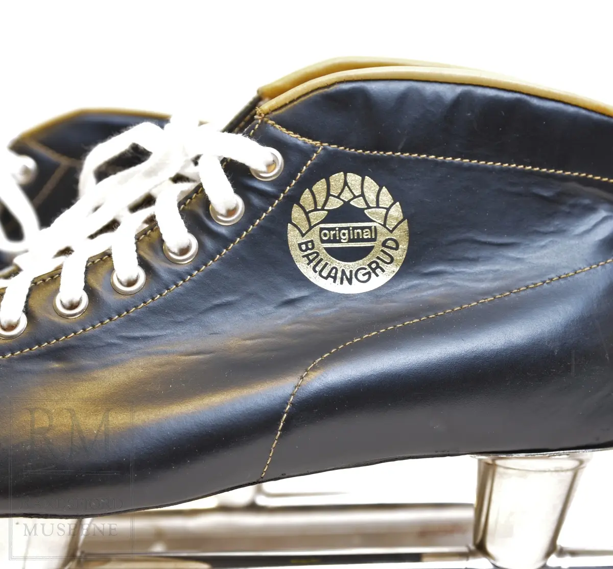 a-b) Skøyter: av svart skinn m / pløse og kant av beige skinn.Røret på skøytejernet avsluttet med plast i begge ender. 
c) plastpose til skøytene.
d) plaststykke.
e-f) Pappeske m/lokk. Brun papp med svart trykk på lokket.
g) pusseklut)
h) skøytefett i tube.