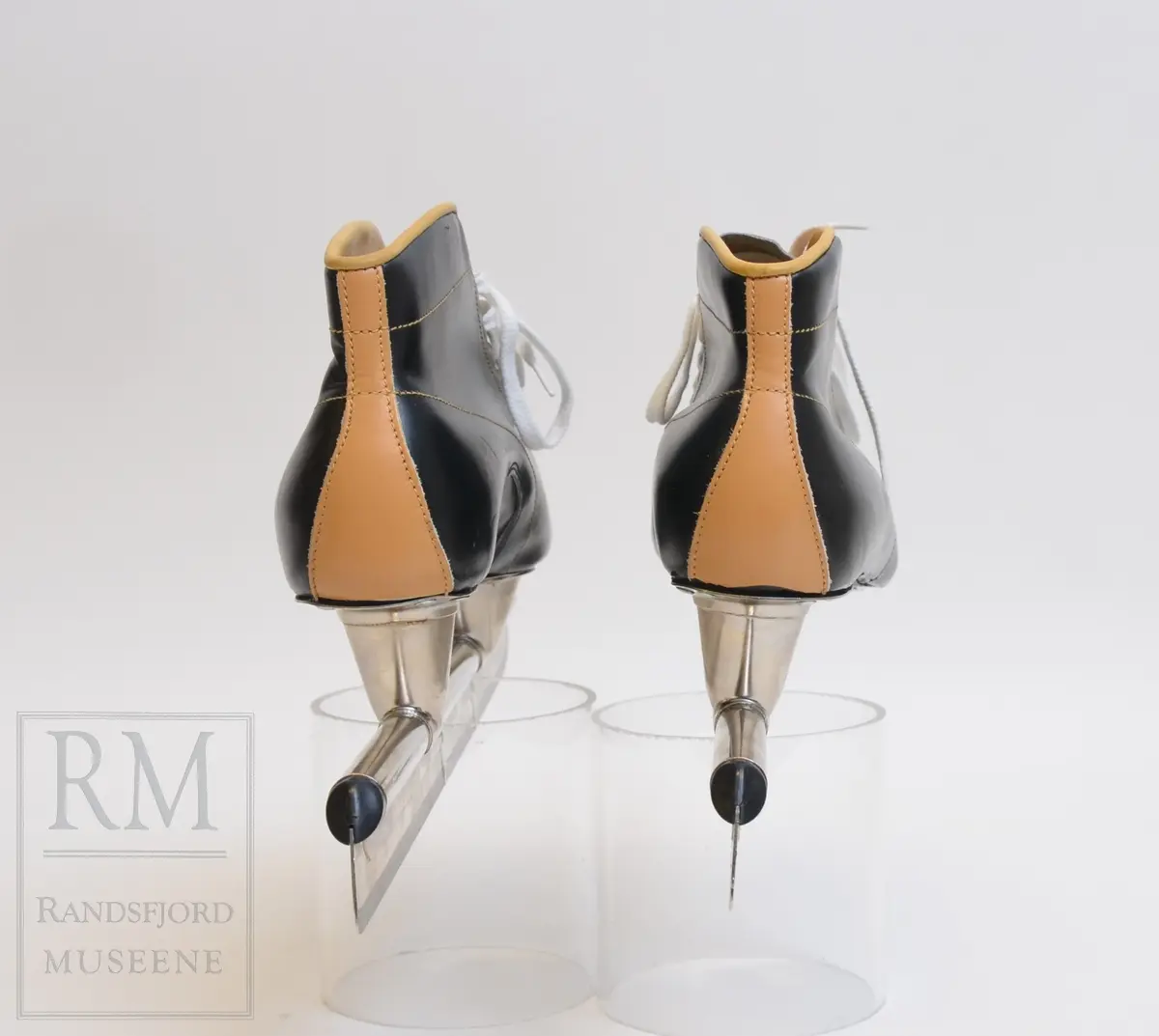 a-b) Skøyter: av svart skinn m / pløse og kant av beige skinn.Røret på skøytejernet avsluttet med plast i begge ender. 
c) plastpose til skøytene.
d) plaststykke.
e-f) Pappeske m/lokk. Brun papp med svart trykk på lokket.
g) pusseklut)
h) skøytefett i tube.