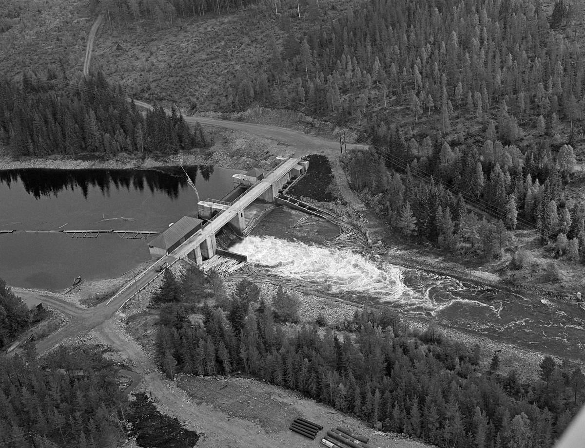 Osdammen, ytterst i Valmen, den vika i den nordvestre enden av Osensjøen i Åmot kommune som leder mot sjøens utløp i elva Søndre Osa. Fotografiet er tatt fra fly. Det viser hvordan vassdraget var lenselagt, og hvordan tømmeret ble fløtt mot Osdammen. Den dammen vi ser på dette bildet ble bygd i 1982-83 av entreprenørselskapet Martin M. Bakken fra Elverum. I motsetning til den forrige dammen fra slutten av 1930-tallet var denne utstyrt med fisketrapp. Bildet viser at fløtingsvirket kunne legge seg i ei bakevje ved nordre elvebredd like nedenfor dammens innløp i Søndre Osa.