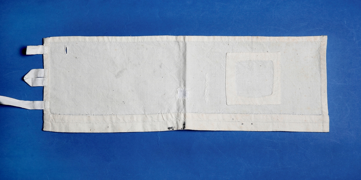 rektangulær prøvelapp i bomullsslerret. Lapping, stopping, knapphull, hemper og påsydd bånd, samt hullsøm og attersøm langs med lappen.