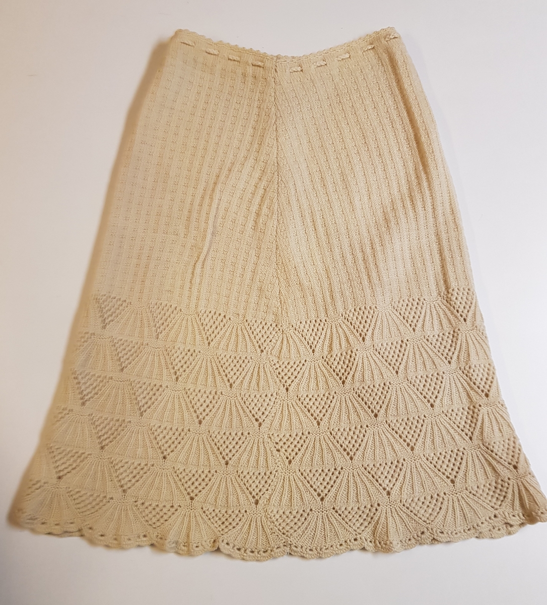 Smalt, men lett utskrådd underskjørt, strikket av gulhvit ullgarn. Hullrad med tvunnet ullsnor i livet, og "stripestrikket" ned til den nedre delen, der skjørtet avsluttes med et bredt parti mønsterstrikket, viftelignende mønster, kantet ytters med en hullbord. Skjørtet har vært omsydd og har søm midt bak med rikelig sømmonn. Sømmen når ned til det viftemønstrede partiet. Skjørtet har også vært sydd inn foran, på hver side, men disse sømmene er smale og gjennomgående helt ned. Pga det vifteformede mønsteret, er sømmene sydd for hånd slik at de følger mønsterets form og ikke bryter vifteformen. Se bildene.