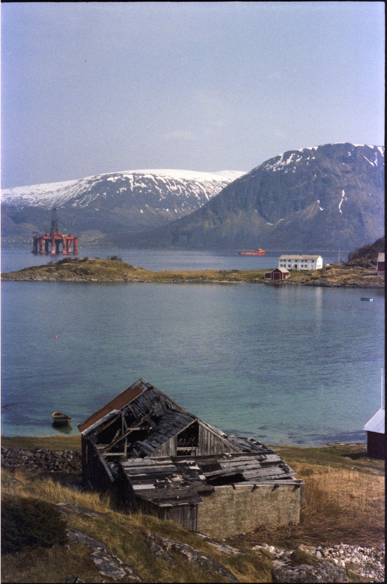 Oljeplattform under slep. Gammelt naust i forgrunnen og Grytøya i bakgrunnen.