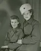 Porträttfoto av två frivilliga luftbevakare ur 91:a ls-kompaniet, stationerade i Tellejåkk, Kåbdalis under beredskapen, 1942. Klädda i uniform. Till vänster Karin Olsson, till höger Karin Nordberg. Klädda i militäruniform.
Serie om två bilder.