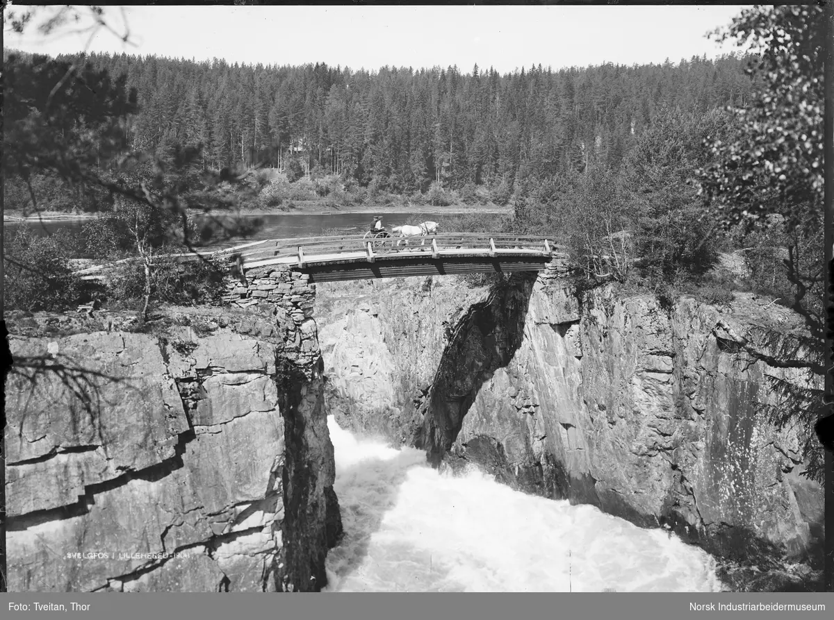 Hest fastspent til vogn, to personer i vogna på trebro over Svelgfossen, trolig like før utbyggingen.