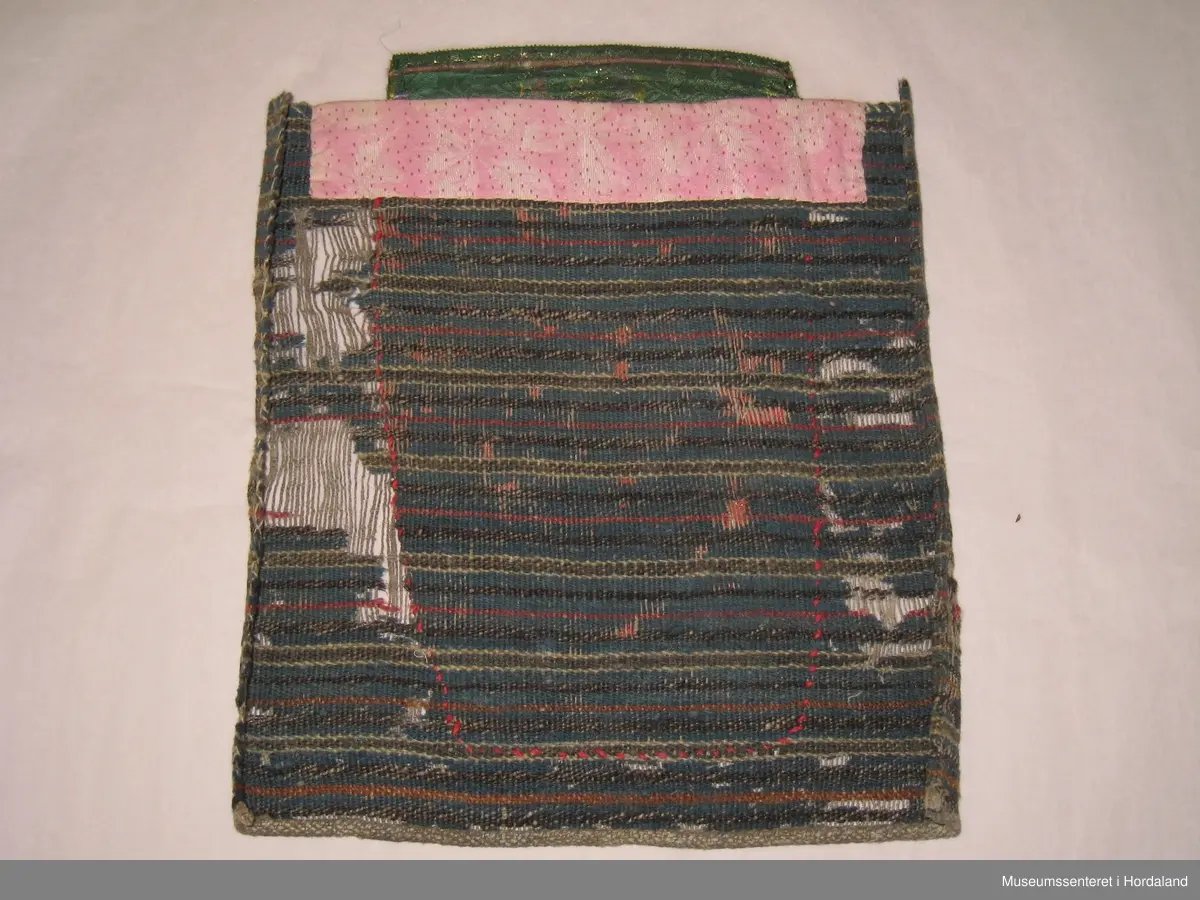 Stor brystduk med perlenett sydd på raudt ullstoff. Nede er det sydd på tre remser av eit anna raudt ullstoff. Montert på eit vove tøystykke der innslagstrådane av ull er borte fleire stader. Renning av heimespunne lin. Kasta over på to sider og falda på to sider med hand. Eit rosa stoff er sydd på oppe til forsterking. Grønt silkeband med rosekvarde og gullfarga metalltråder vove inni er montert utanpå det rosa stoffet øvst.