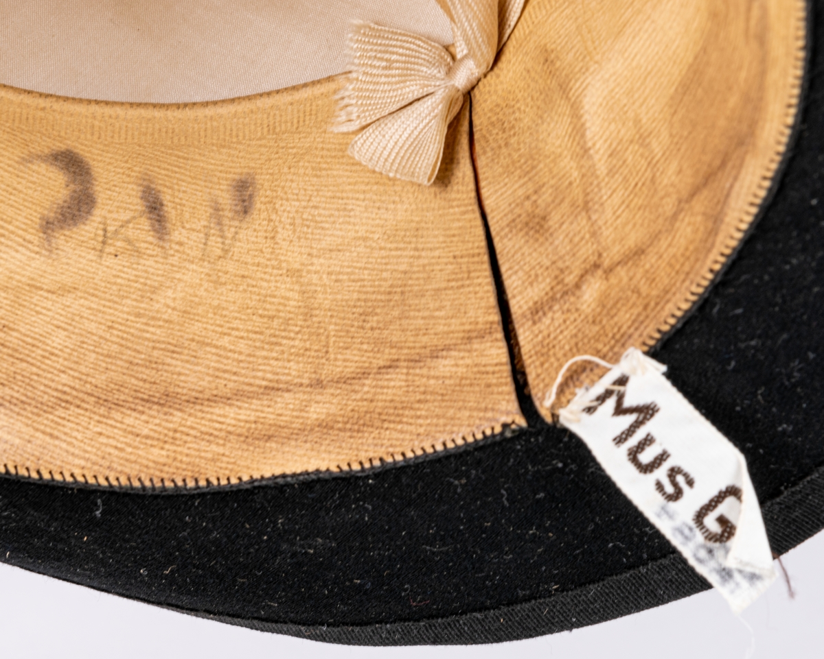 Stormhatt märkt Aktiebolaget J.W Haglund, N. Kungsgatan 1, Gefle. Svart.
Höjd 14cm, brättbredd 4,5cm.
Hattask av svart papp med guldtext på locket. English manufacture of hats. Best London deposed.