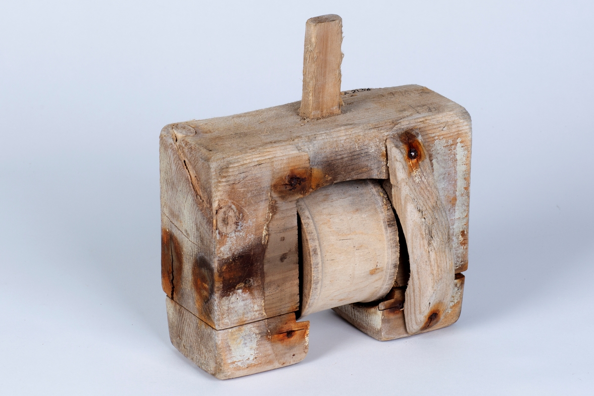 En firkantet tregjenstand med en trommel i midten som går rundt. Satt sammen med spiker.