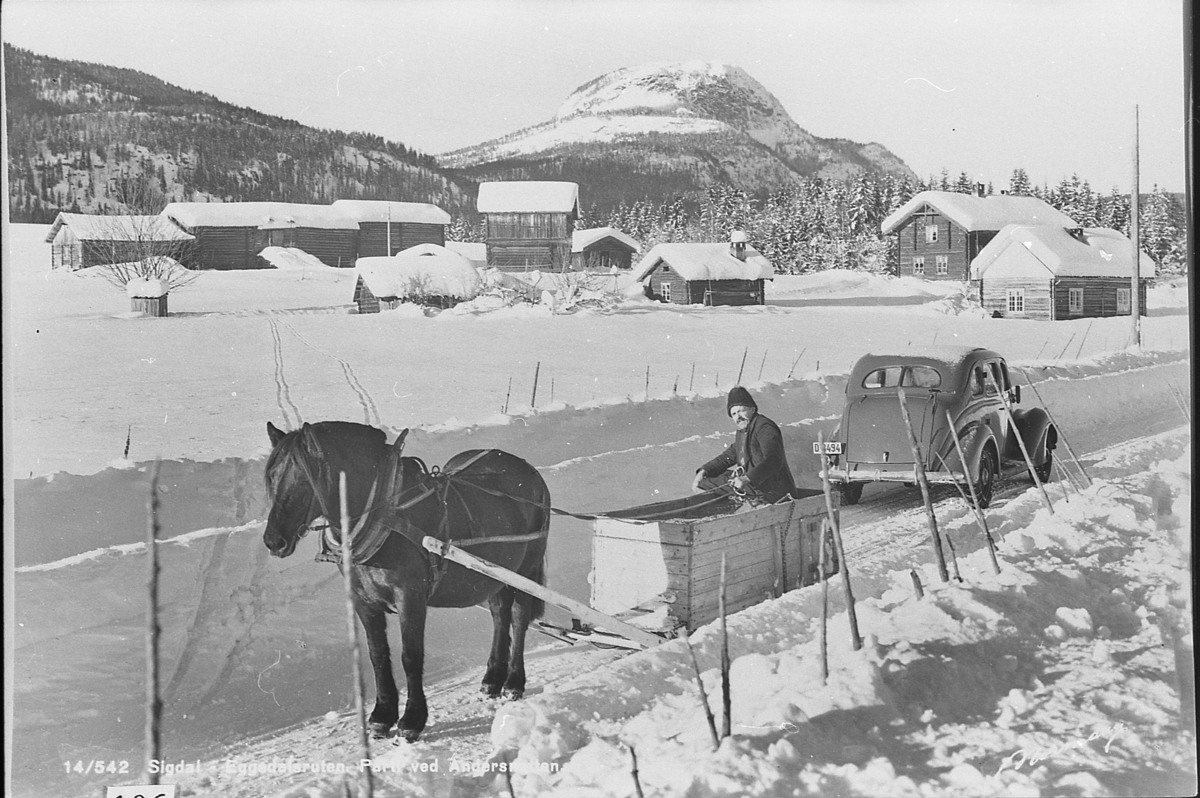 Gruskjøring med hest og kasseslede. Kjørekar: Anders T. Weggesrud (1881-1954).
Bil av førkrigsmodell. Båsum, Nedre. Andersnatten i bakgrunn.
Prospektkort med tekst "Sigdal-Eggedalsruten. Parti ved Andersnatten"