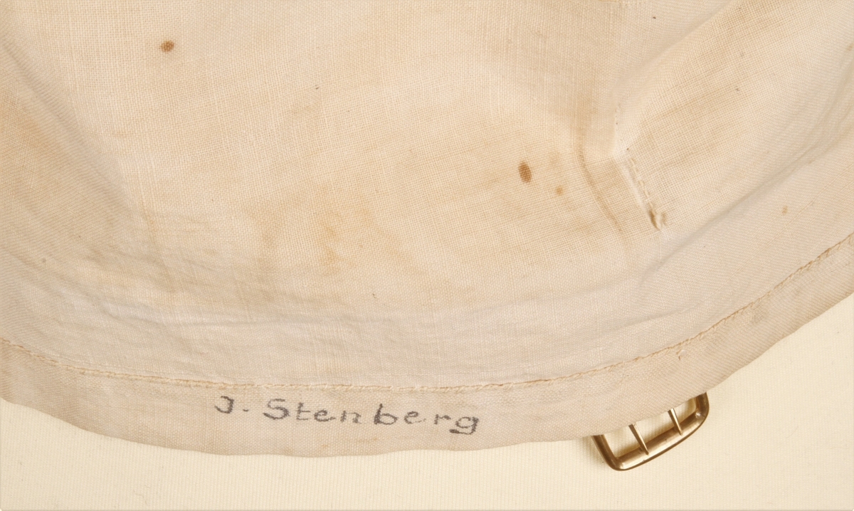 Vest sydd i rutet stoff med jordfarget bunn, lyseblå og brune striper som danner ruter. Vesten er enkeltspent og har seks knapper. Én stikklomme på hvert forstykke. Spensel i ryggen som er festet med en gullfarget metallspenne. Hele vesten er håndsydd. 