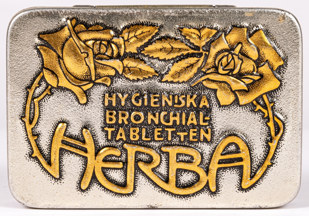 Tablettask i plåt, silverfärgad botten med rosdekor och text i guld: "HYGIENISKA BRONCHIALTABLETTEN HERBA".