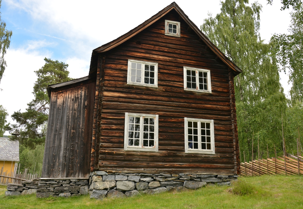 Bygning i to høgder, med sval og rosemåla dører.