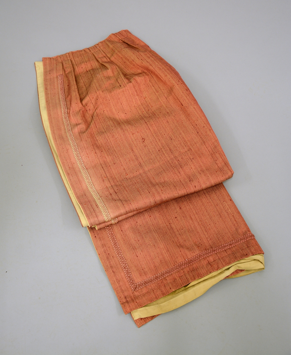 Gardin med kappe og stores. Rødorange gardin i bomull og syntetiskematerialer. Gardinen er fòret med beige bomullstøy. Gardinkappe i samme materiale. Rosa stores i bomull. Gardinen har hengt i spisesalen på Ulefos Hovedgaard.