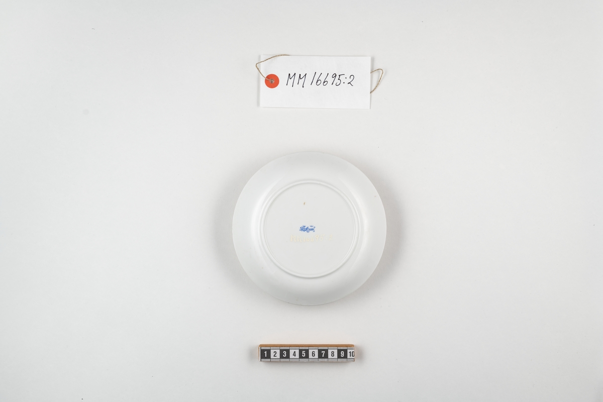 Cylindriskt fat i vitt porslin. Dekorerat med lilla riksvapnet samt därunder texten: " H M Sverige ". Dekoren utfört i blått. På undersidan stämplat i blått: Rörstrand. Dessutom ett påklistrat munlack i blått med vit text enligt följande: Karl Björkmans Jern-Glas- & Porslinshandel Ronnebygatan 36 Karlskrona.