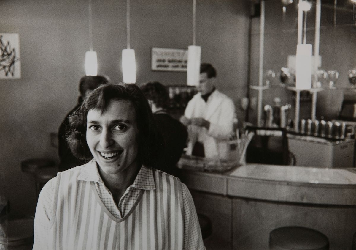 Katarina Taikon (1932-1995) var författare och samhällsdebattör och ledande gestalt i romernas medborgarrättsrörelse under 1960- och 1970-talen. Här syns hon på Vips American Ice Cream Bar, som hon förestod i början av 1960-talet. Taikon beskrev utifrån egna erfarenheter svenska romers liv och villkor i Sverige i såväl skön- som facklitterär form. Efter utgivningen av sin debutbok Zigenerska (1963) kom hon att bli ansiktet utåt för romers rättighetskamp i Sverige. Hon var aktiv i Zigenarsamfundet och tog 1966 över utgivningen av samfundets opinionsbildande tidskrift, Amé Beschás, (senare Zigenaren) tillsammans med sin man fotografen Björn Langhammer. Langhammer kom att dokumentera stora delar av Katarina Taikons kamp och romers sociala situation. År 1969 publicerade Taikon sin första barnbok om den romska flickan Katitzi, då hon ansåg att om man ville förändra samhället måste man börja med barnen. Fram till 1980 publicerades tolv böcker i samma serie och böckerna har även utkommit som tv-serie, serietidning och på LP-skiva. År 1982 fick Taikon ett hjärtstillestånd vid ett läkarbesök och kom att ligga i koma intill sin död 1995. Katarina Taikon var syster till silversmeden Rosa Taikon, som fortsatte kampen för romers rättigheter efter systerns bortgång.