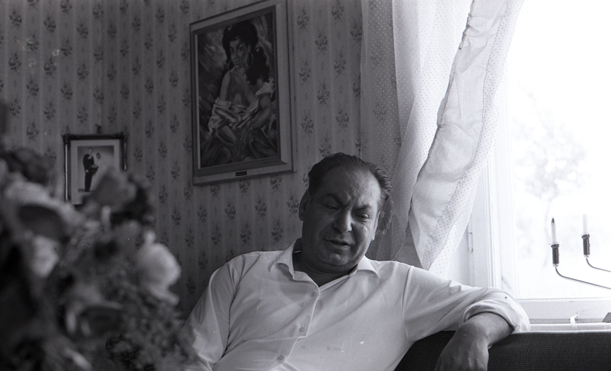 En man sitter i sitt vardagsrum och blir intervjuad av en journalist. Bilden är tagen i samband med ett nyhetsreportage för Skånska Dagbladet. Efter att de svenska romerna i Sverige erkändes som medborgare år 1952 uppstod debatt kring gruppens svåra levnadsförhållanden.