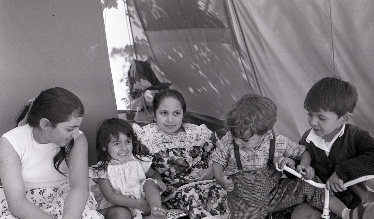 Några romska barn poserar framför kameran i Malmö sommaren år 1963. Bilden är tagen i samband med ett nyhetsreportage för Skånska Dagbladet. I reportaget porträtteras en romsk familj och hur de trivs med att ha blivit bofasta.