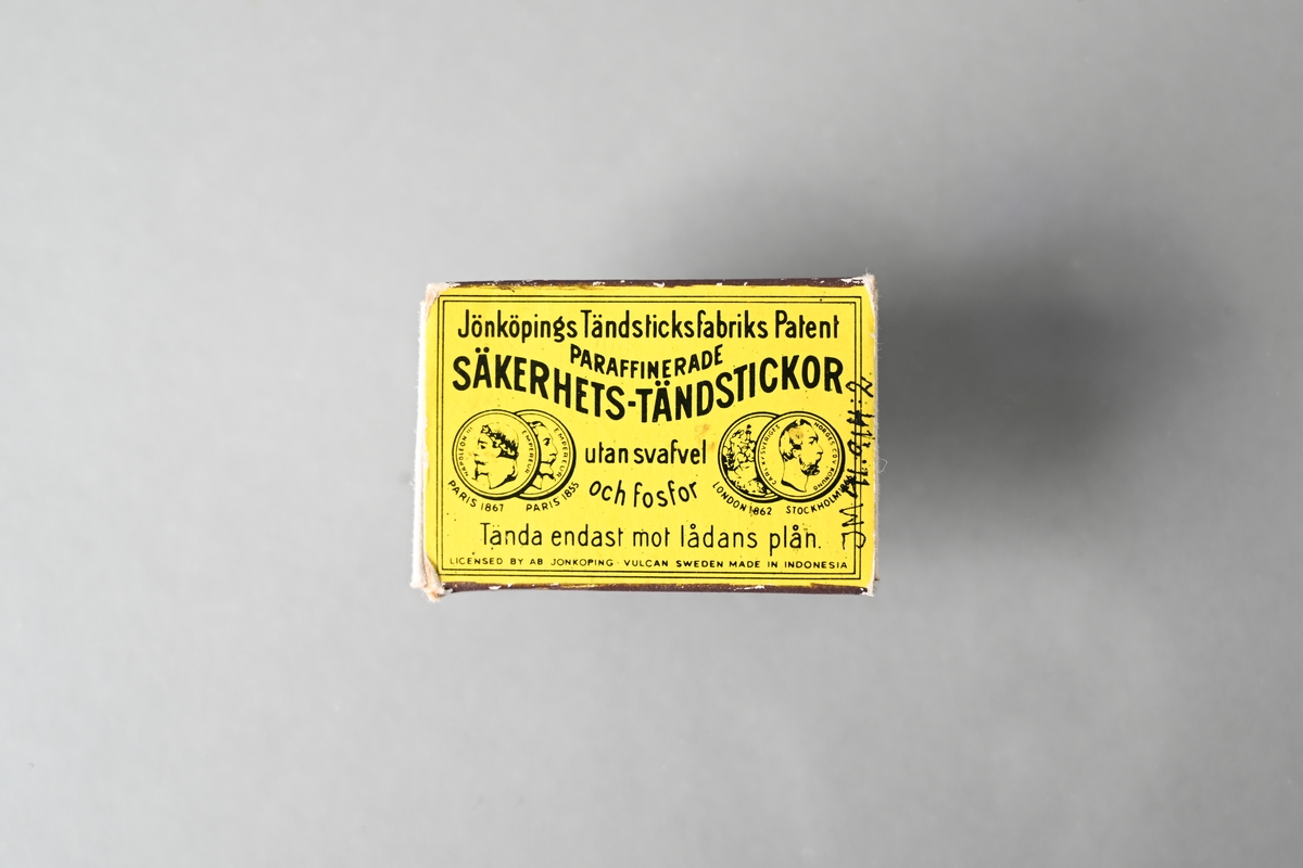 Tändsticksask bestående av innerask och ytterask. Ytteraskens ovansida är gul och har tryckt text: "Jönköpings Tändsticksfabriks Patent PARAFFINERADE SÄKERHETS-TÄNDSTICKOR utan svafvel och fosfor Tänd endast mot lådans plån LICENSED BY AB JÖNKÖPING-VULCAN SWEDEN MADE IN INDONESIA". På ytteraskens ovansida finns även tryckta bilder av medaljer från utställningar i Paris 1855 och 1867, och utställningar i London 1862 och Stockholm 1866. Ytteraskens undersida är blå. Asken innehåller nio oanvända tändstickor.

JM 41914:1, innerask
JM 41914:2, ytterask