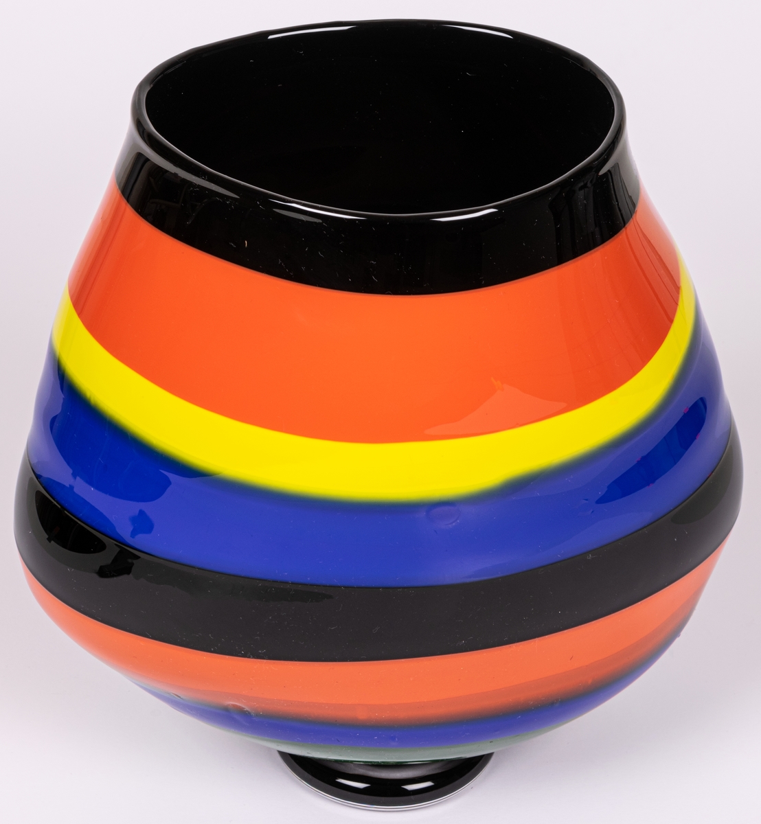 Vas, blåst, med pålagda färgfält, modell "Mali". Oregelbundet oval, bukig i längdled. Tvärrandig i svart, orange, gult och blått. Avrundad mot smal, tjock fot. Märkt under: "Utställning".