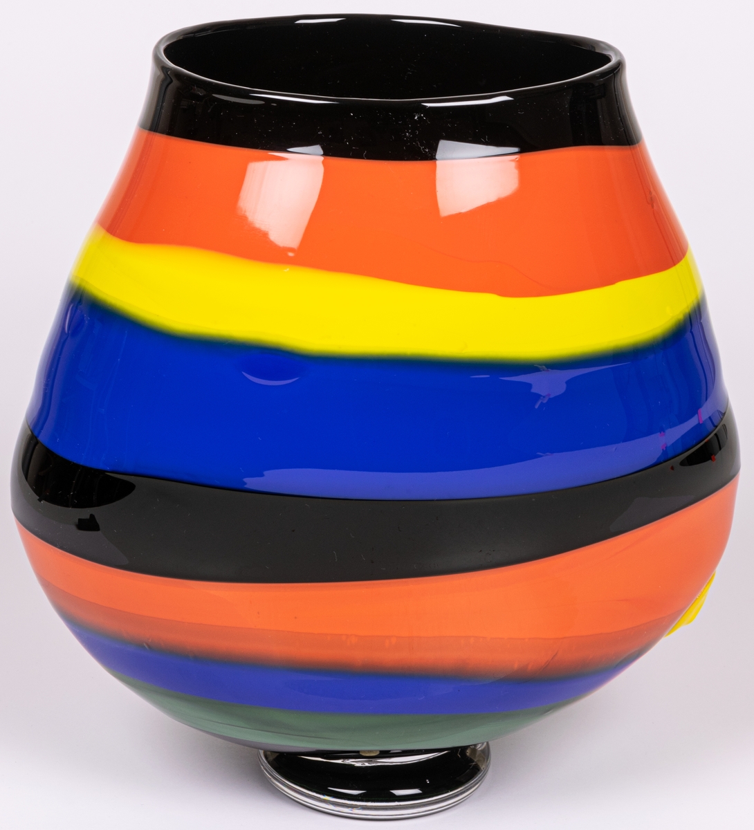 Vas, blåst, med pålagda färgfält, modell "Mali". Oregelbundet oval, bukig i längdled. Tvärrandig i svart, orange, gult och blått. Avrundad mot smal, tjock fot. Märkt under: "Utställning".