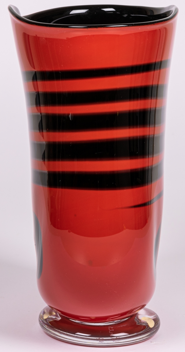 Vas, blåst, med pålagda färgfält, modell "Mali". Tillplattat oval. Röd med sex svarta tvärränder ovan en svart oval. Rundad nedtill mot smal, ofärgad fot.