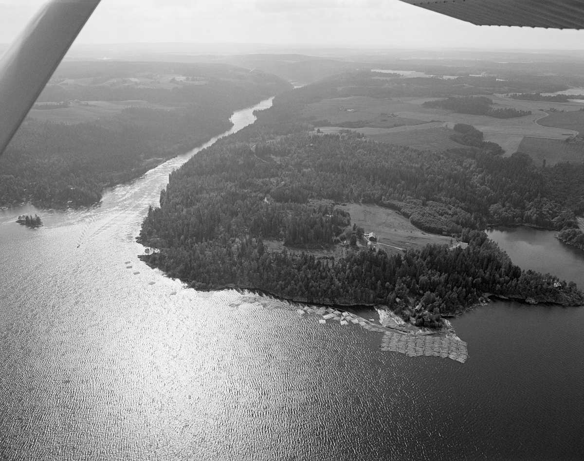 Flyfotografi fra Sleppetangen i Spydeberg i Østfold.  Bildet er tatt fra øst mot vest.  Til høyre i bildet ser vi fløtersenteret ved Sleppetangen, der det lå et tømmerslepp, som man øyensynlig var i ferd med å løse opp.  Tømmeret drev mot nedre Glomma og Mørkfoss.  Helt til høyre i bildet ser vi ei bukt, Bogen.  Det som skjedde ved Sleppetangen var at slepene og «mosene» (tømmerbuntene) det var sammensatt av, ble løst opp, slik stokkene kunne drive løse mot elveløpet.  Tømmeret kunne nemlig ikke passere tømmerrennene ved de nedenforliggende kraftverkene i «moser». 