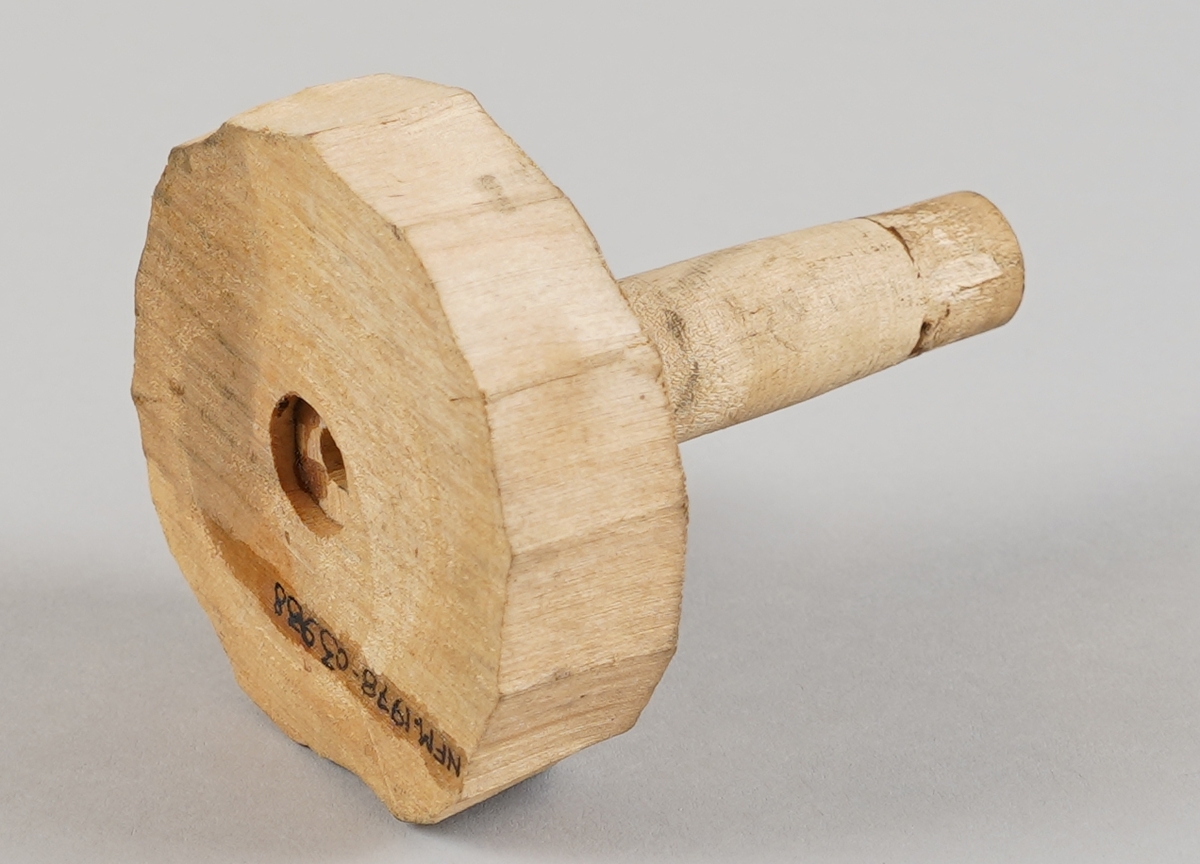 Emne til snelle (som er del av tein til hjulrokk) der eine klossen er borte.  Eit dreia stykkje er sett ned i ein tilnærma sirkelforma kloss i eine enda. Det er hol gjennom dei to delane i senter.