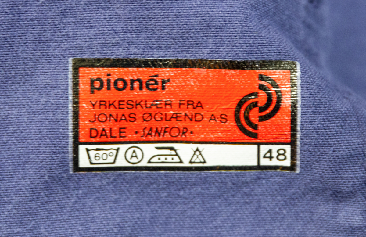 Todelt dress i mørk blå bomullsdenim. Storleik 48 (båe delene). Glidelås i metall framme i jakke, knepping med metallknappar i buksegylf. To brystlommer på jakka, to stikklommer i buksa. Innside av bukselinning i tynt nylonstoff (?). Buksa har produsentmerket laminert fast i høgre lomme og jakka har tilsvarande på innsida bak høgre brystlomme. Vaskeanvisning 60 gr. 

Buksa har fleire større og mindre hol, særleg nede på venstre buksebein, - både framme og bak. Om desse er forårsaka av varme eller syre er ikkje kartlagt, men fargen tyder på høg varme. Det er ikkje gjort forsøk på reparasjon av hola. Stoffet er ikkje flammehemma.
