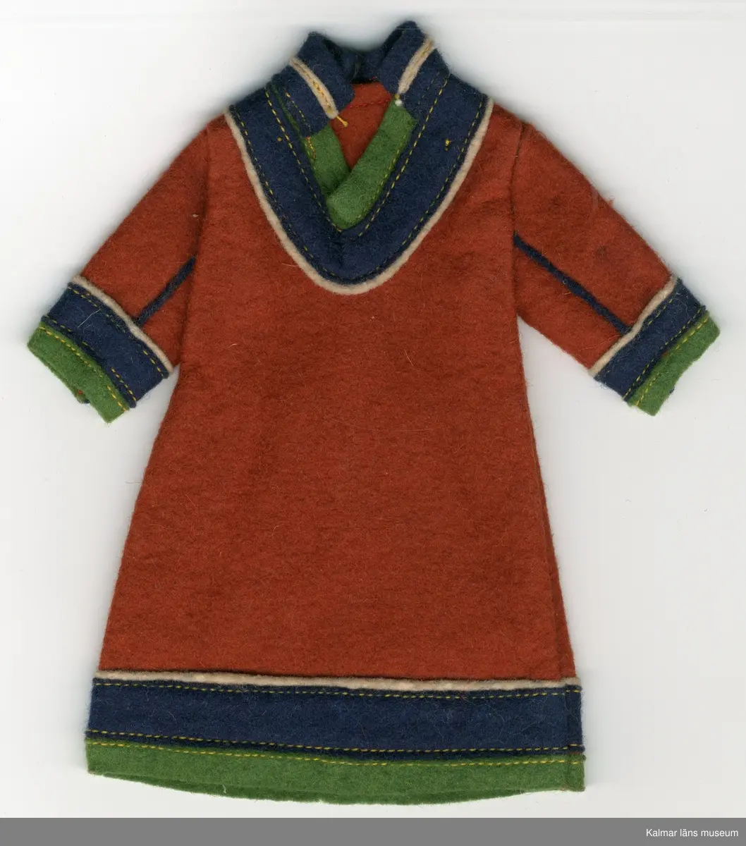 KLM 28082:292:1-3 Samekolt, dockkolt, 3 stycken, av textil, ylle. Lång kolt, utan öppning, brun, med grön, mörkblå och vit garnering. Nertill på ärm och koltens fåll, tygränder, lodräta, vit, mörkblå och grön, i nämnd ordning. Längs ärm, två blåa ränder i tyg, passepoalsydda. Krage, blå, hög i nacke, med vit tygrand, framtill, v-krage, i grönt, blått och vitt tyg. Del av samisk nationaldräkt.