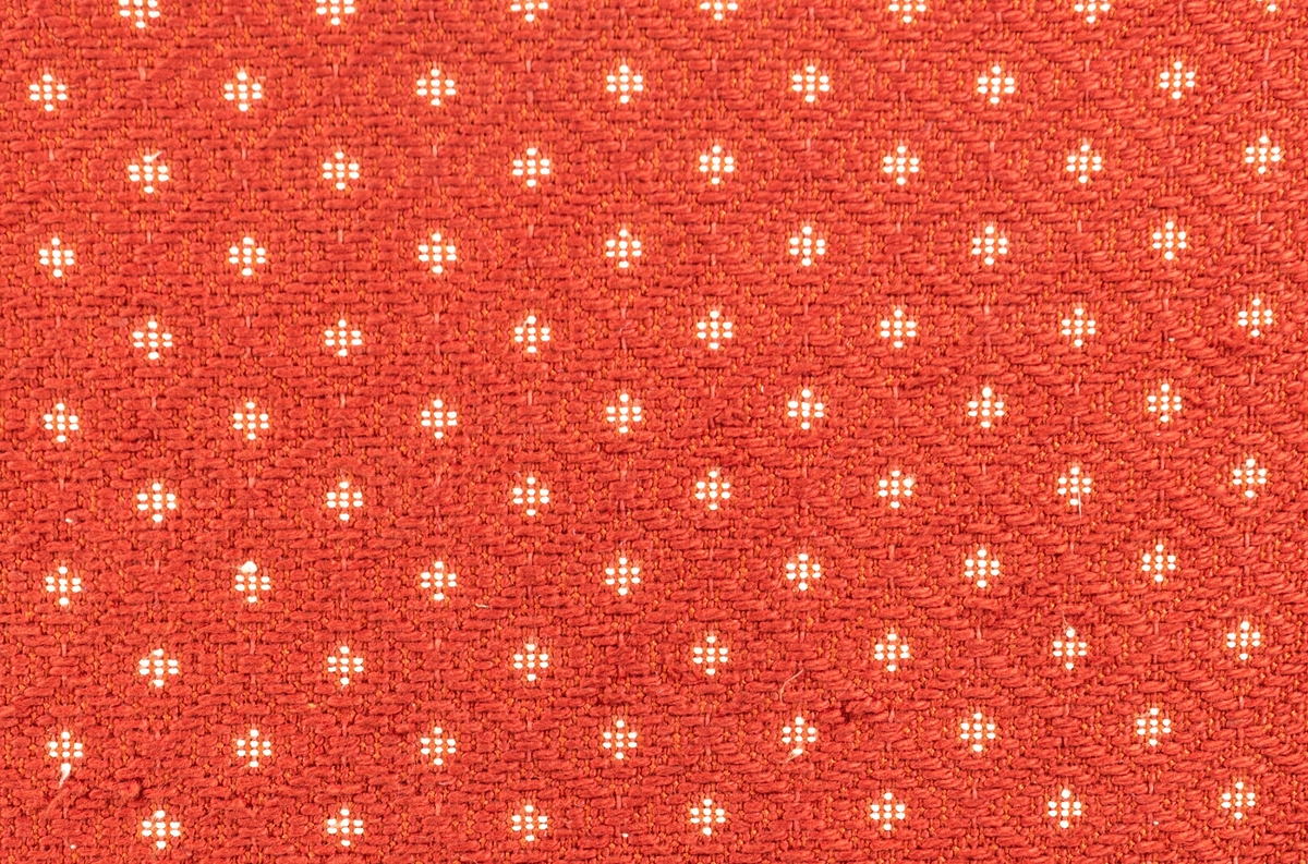 Katalogkort: Fåtölj. Ljust träslag i armstöd och ben. Sits och ryggstöd klädda med mönstervävt tyg. Varp: röd. Inslag: rett, vitt. Gåsögonliknande mönster. Sitsens kant, kantad med snodd i rött och vitt. På stolsryggens framsida fanns ursprungligen 3 textilklädda knappar, varav en saknas.

h 80cm, b 66cm, dj 77cm