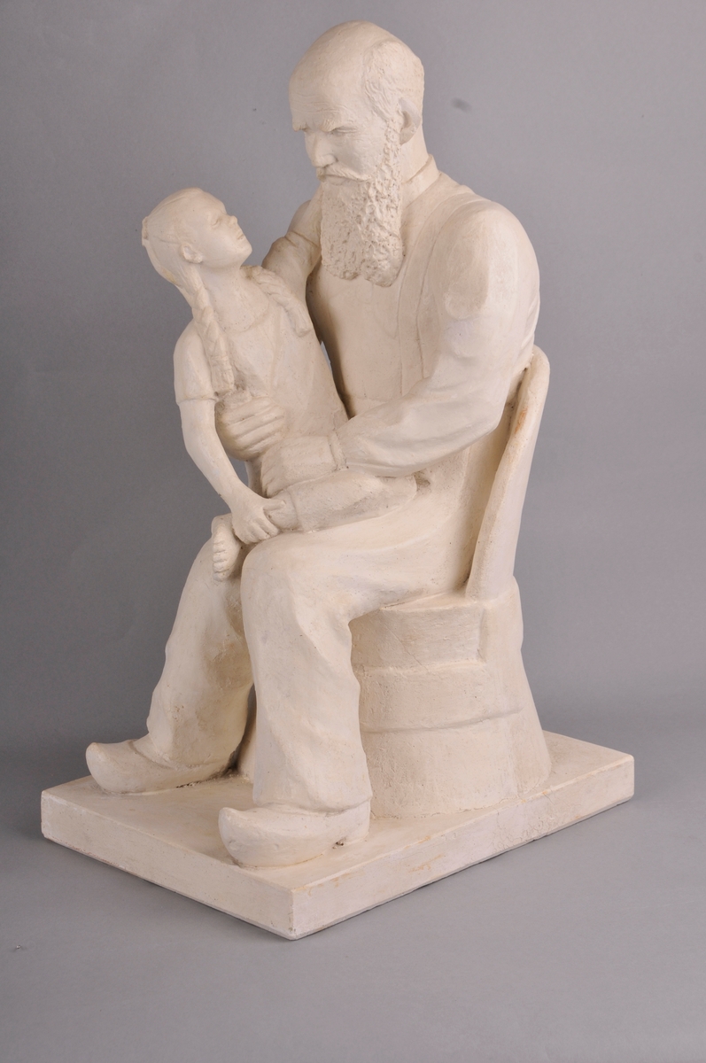 Gamal mann med heilskjegg. Mannen sit i ein kubbestol og har tresko på føtane. Ein berrføtt jentunge med fletta hår sit på fanget og ser bestefaren i andletet. Tittel: "Bestefar fortel."