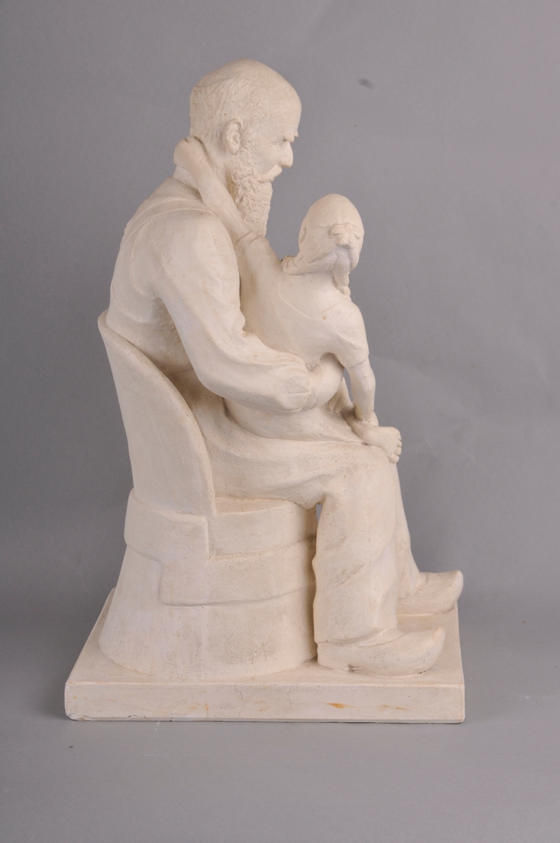 Gamal mann med heilskjegg. Mannen sit i ein kubbestol og har tresko på føtane. Ein berrføtt jentunge med fletta hår sit på fanget og ser bestefaren i andletet. Tittel: "Bestefar fortel."