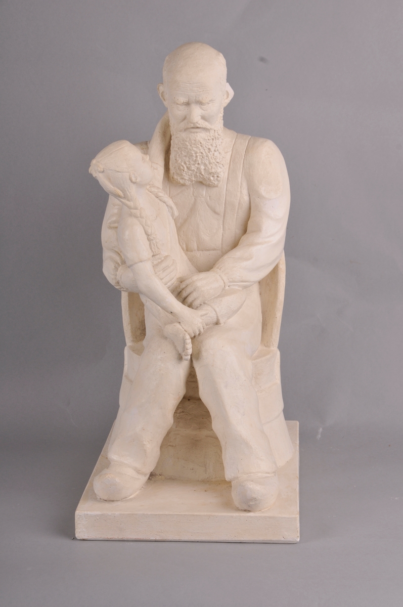 Gamal mann med heilskjegg. Mannen sit i ein kubbestol og har tresko på føtane. Ein berrføtt jentunge med fletta hår sit på fanget og ser bestefaren i andletet. Tittel: "Bestefar fortel."