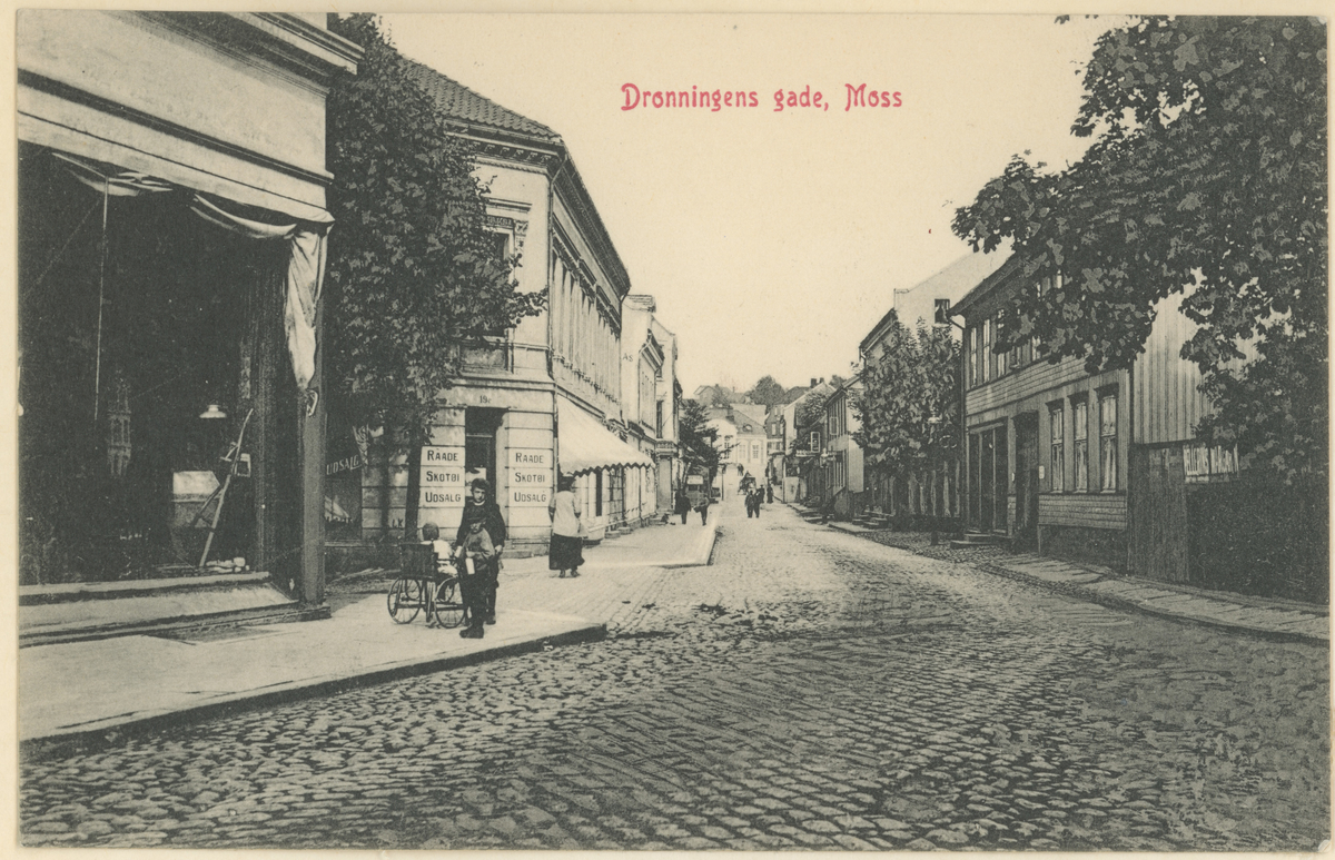 
Dronningens gate. Postkort.
Ca. 1910. Fotograf har stått i Dronningens gate ved "Kirkeparken videregående".
Detaljer:	Raade Skotøiutsalg i nummer 19 venstre side. Thodberggården på høyre side.
Historikk: Det meste på bildet står fortsatt i dag.
.
Tekst: "Dronningens gade, Moss"
