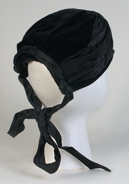 Av svart sammet med två 550 mm långa , svarta knytband av siden bak jämte svart resårband. 
Mått: 113 x 135 mm.