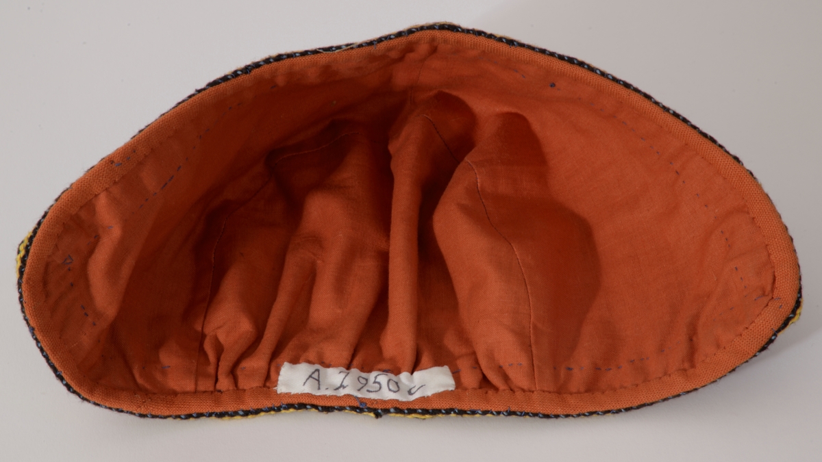 Vestfoldbunad 1932 modell, bomull. Stakk: Maljer med masker og tvunnet snor, flerfargede bånd om ermer, hals og skjørt, belte med  sirkelformet sølvspenne til å hekte, gravert dekor.  Forkle, litt nedsydde legg i livet, flettet rødbrun snor med dusk i endene, mønstervevd bord i gult/brunt nede.  Lue, D-form, bakstykket rynket nede, kantet med bånd, rødbrunt for.