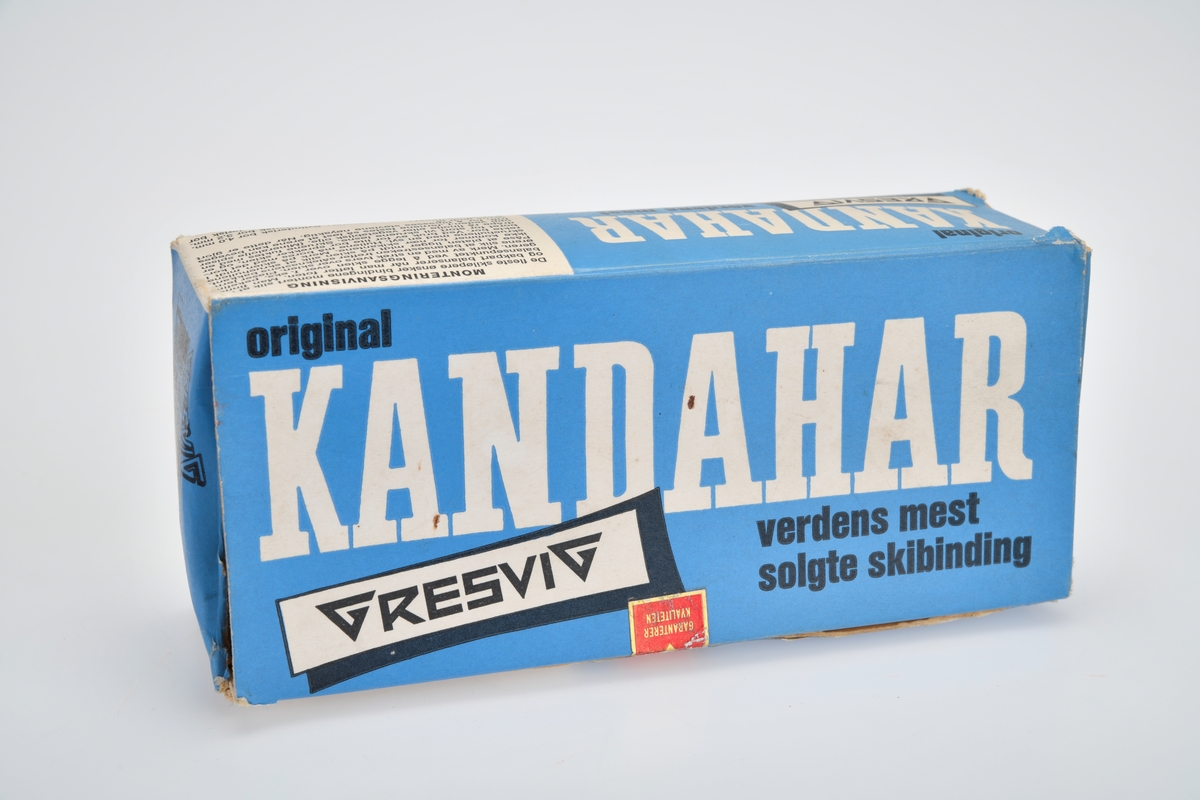 En eske med et par skibindinger av typen "Kandahar". Esken er laget av papp med lokk som åpnes fra toppen. Lokket henger fast i esken på den bakre delen av esken. Esken er blå med skrift i svart og hvitt. For tekst, se "Påført tekst/merker". På hver langside av esken står det monteringsanvisning trykt. På den ene kortsiden er det et bilde av Gresvig Sportsartikkel Fabrikk. På den andre siden står nummeret på bindingen samt prisen som var 45,-nok (skrevet på med blyant). I esken ligger det i alt 14 deler til skibindingen samt to poser med ulike skruer og fester. Kandaharbindingen er en skibinding bestående av en vaier som går fra en strammemekanisme foran skiskoen, rundt skoen bak hælen og tilbake til strammemekanismen.