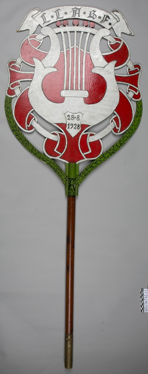Emblem med motiv av strenginstrumnt lyre. Samme motiv på begge sider av emblem.