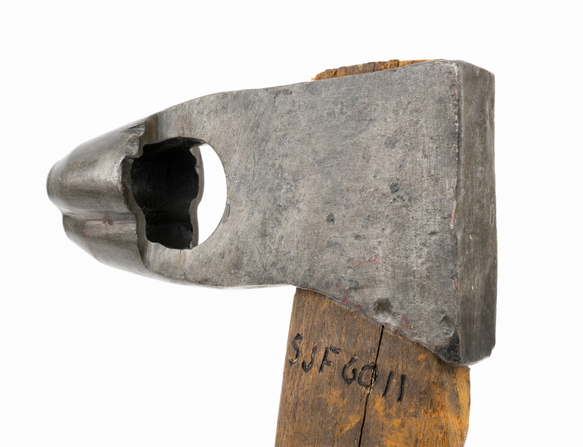 Merkeøks med ubehandlet askeskaft. Øksebladet er 13,8 centimeter høyt fra egg til nakke, og det noenlunde rektangulære nakkepartiet (hammeren) måler 7,6 X 2,7 centimeter. Øyet (skafthullet) er 4,3 centimeter høyt og opptil 1,5 centimeter bredt i forkant, noe romsligere i bakkant. På den nedre delen av bladgodset er det en U-formet utsparing som har fungert som sponrom for «merkedelen», et cirka 3,8 centimeter høyt element med profilert egg som er sveiset fast til «beina» (smeden kalte dem «stabler») på «U-en». Den profilerte eggen er fasslipt utvendig. Den er formet som et trefliket blad. Øverst på høyre side av øksebladet finner vi smeden stempel - «K. KNUDSEN MJØNDALEN» med to sirkulære avbildninger av medaljer produsenten sannsynligvis har høstet på utstillinger ved siden av. Dette tyder på at øksa kan være smidd av Karl Henrik Knudsen (1870-1956) eller eventuelt sønnen Oddmund Knudsen (1900-1983), som fortsatte å bruke farens stempel de første åra han drev smia. 

Skaftet er drøyt 61 centimeter langt (inkludert den delen som er skjult i øyet på øksa). Det er rett, og som økseskaft flest ganske flatt og bredt i den fremre enden og noe mer rundovalt baker. Forbindelsen mellom bladet og skaftet er gjort tettere og fastere ved hjelp av en trekile i skaftenden. Kilen er lysere i veden og nyere enn skaftet for øvrig. Navnet til firmaet som fikk det tømmeret det kjøpte i Numedalslågens nedslagsfelt merket med denne øksa - «Norsk Impregneringsco» - er påført høyre skaftside med grov svart tusj. Denne bedriften lå i Larvik.  På merkekartet for Numedalslågen fra 1960 har denne øksa nummer 19, og den knyttes til Asbjørn Danielsens navn. Dette eksemplaret var det Lågen Tømmermåling i  Larvik som forvaltet.

Bladet later til å ha vært demontert og rustbehandlet etter at det kom til museet. Skaftet er sprukket. Dette er sannsynligvis en gammel skade.
