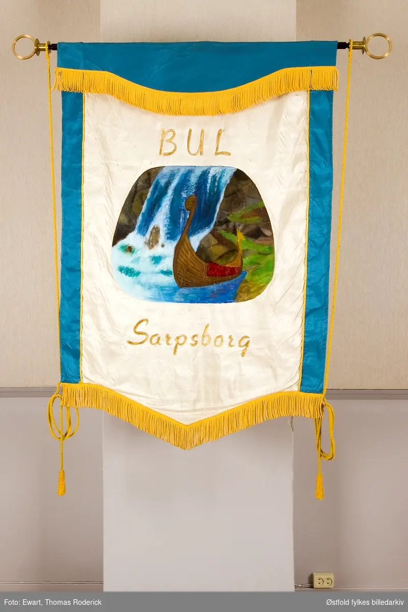 Fane  til BUL Bondeungdomslaget i Sarpsborg, stiftet 14.oktober 1915. Forside.
Tekst på bakside:
Bondeungdomslaget i Sarpsborg skipa 14. oktober 1915.
