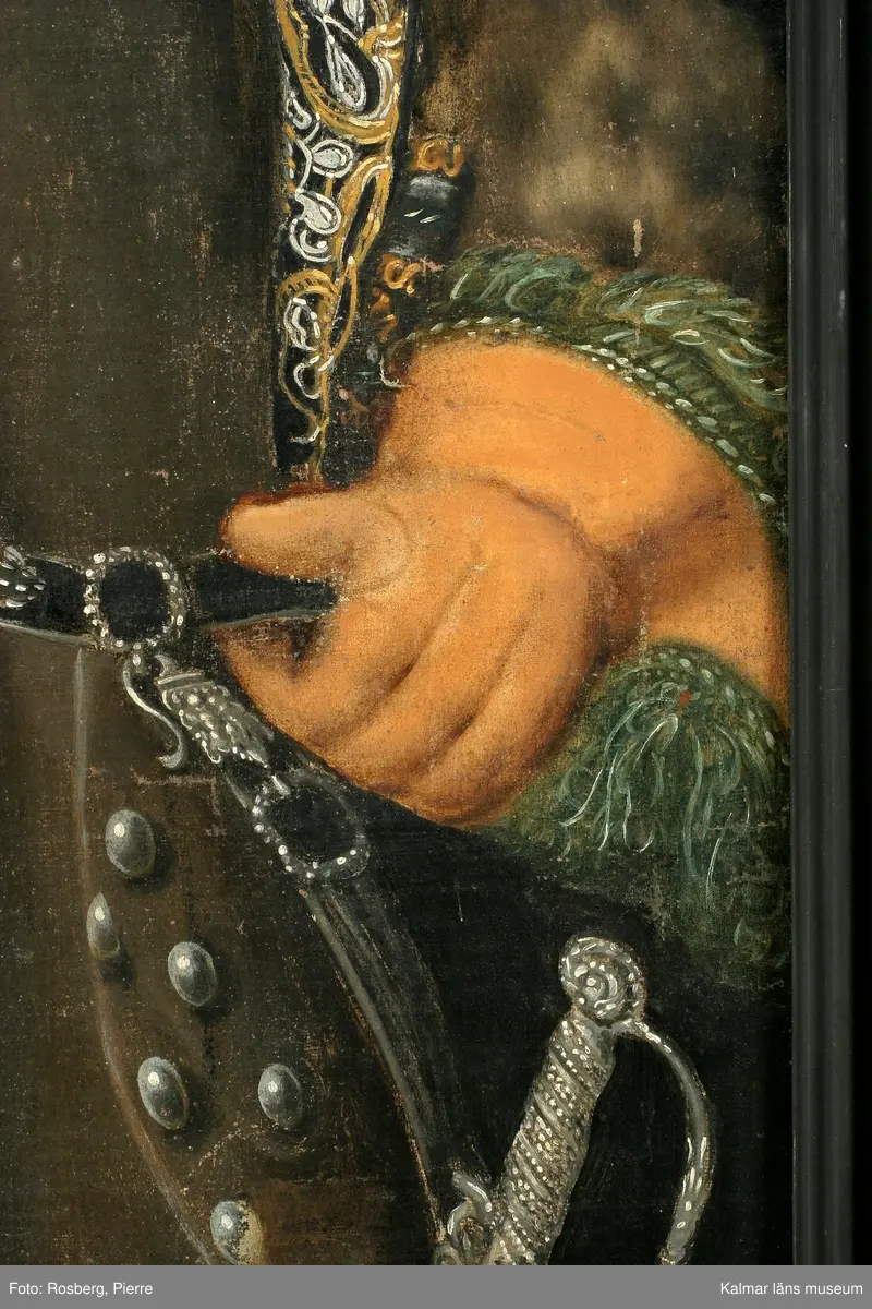 Porträtt av Magnus Gabriel Craelius, Fortifications-Capitain i Kalmar. Grön livrock av polskt snitt. Skinnuppslag på ärmarna. Stora ficklock med många knappar. Värja och gehäng. Spetskrås vid hals mm. Peruk. I högra handen käpp och handske, på vänstra handen älghudshandske.
