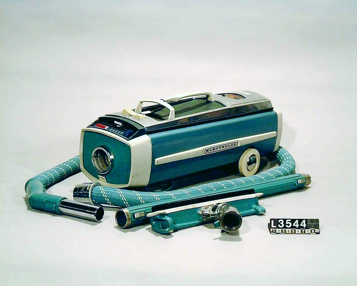 Blå metallicfärgad dammsugare på hjul med fram och bakparti i vit plast. Stötdämpare i plast med Electrolux på sidan. Slang, rör och munstycke följer maskinens färgskala. Dammsugaren har kabelvinda, dammindikator och dammbehållare i papper.