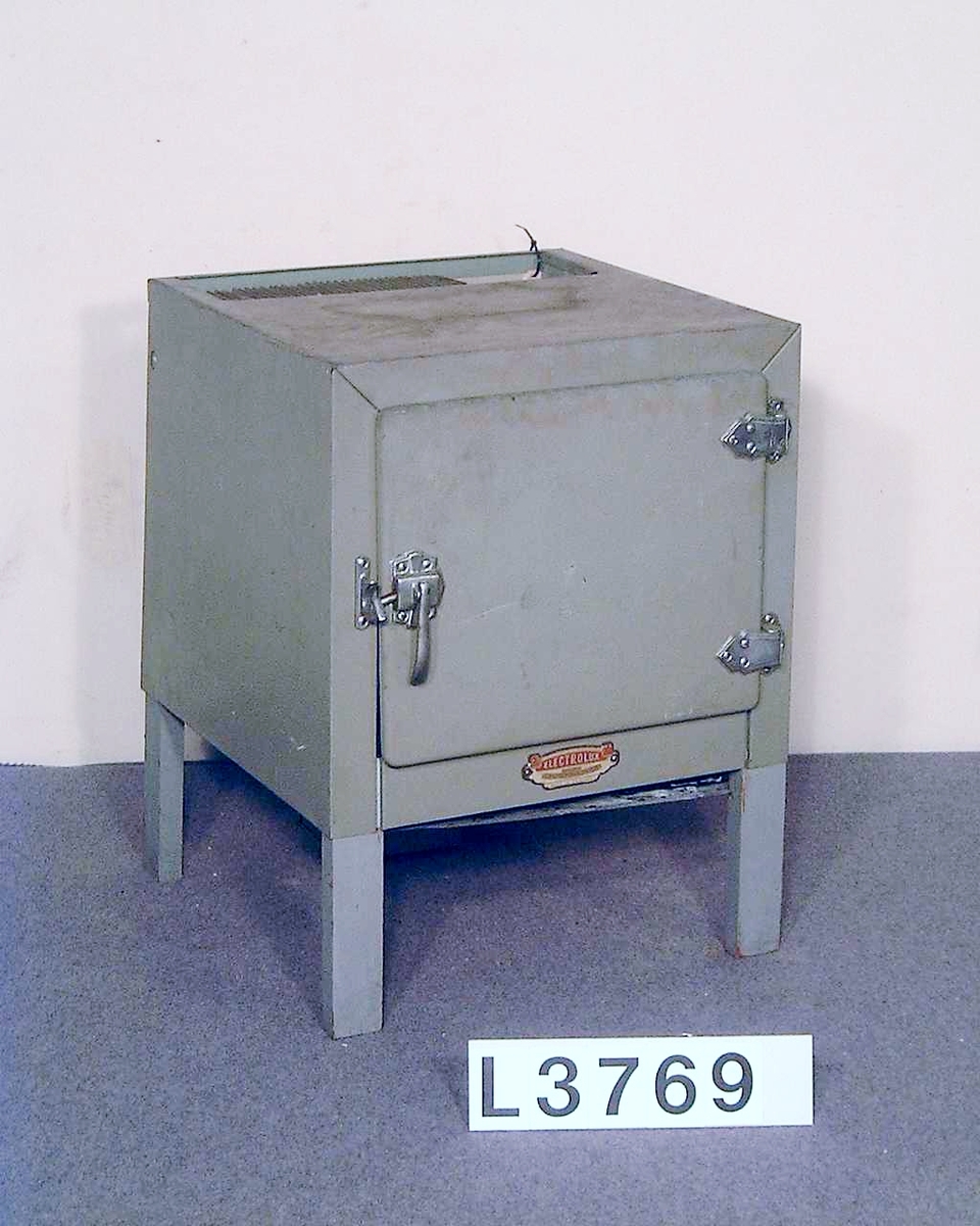 Litet kylskåp i grå/grön metall, absorptionsmodell med utrustning för stadsgas. Under dörren finns en skylt med följande inskription: "Electrolux the gas refrigerator. Made in England."