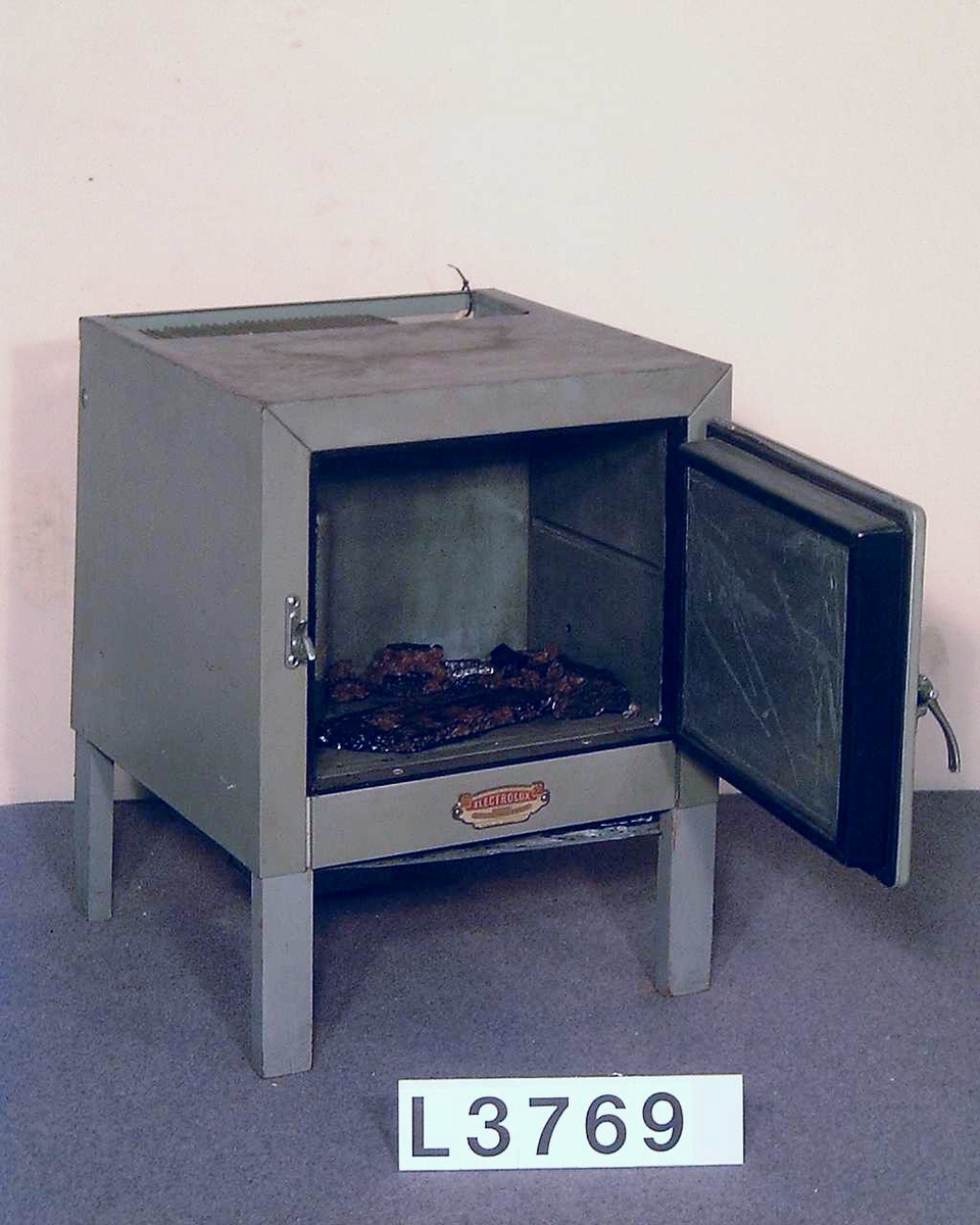 Litet kylskåp i grå/grön metall, absorptionsmodell med utrustning för stadsgas. Under dörren finns en skylt med följande inskription: "Electrolux the gas refrigerator. Made in England."