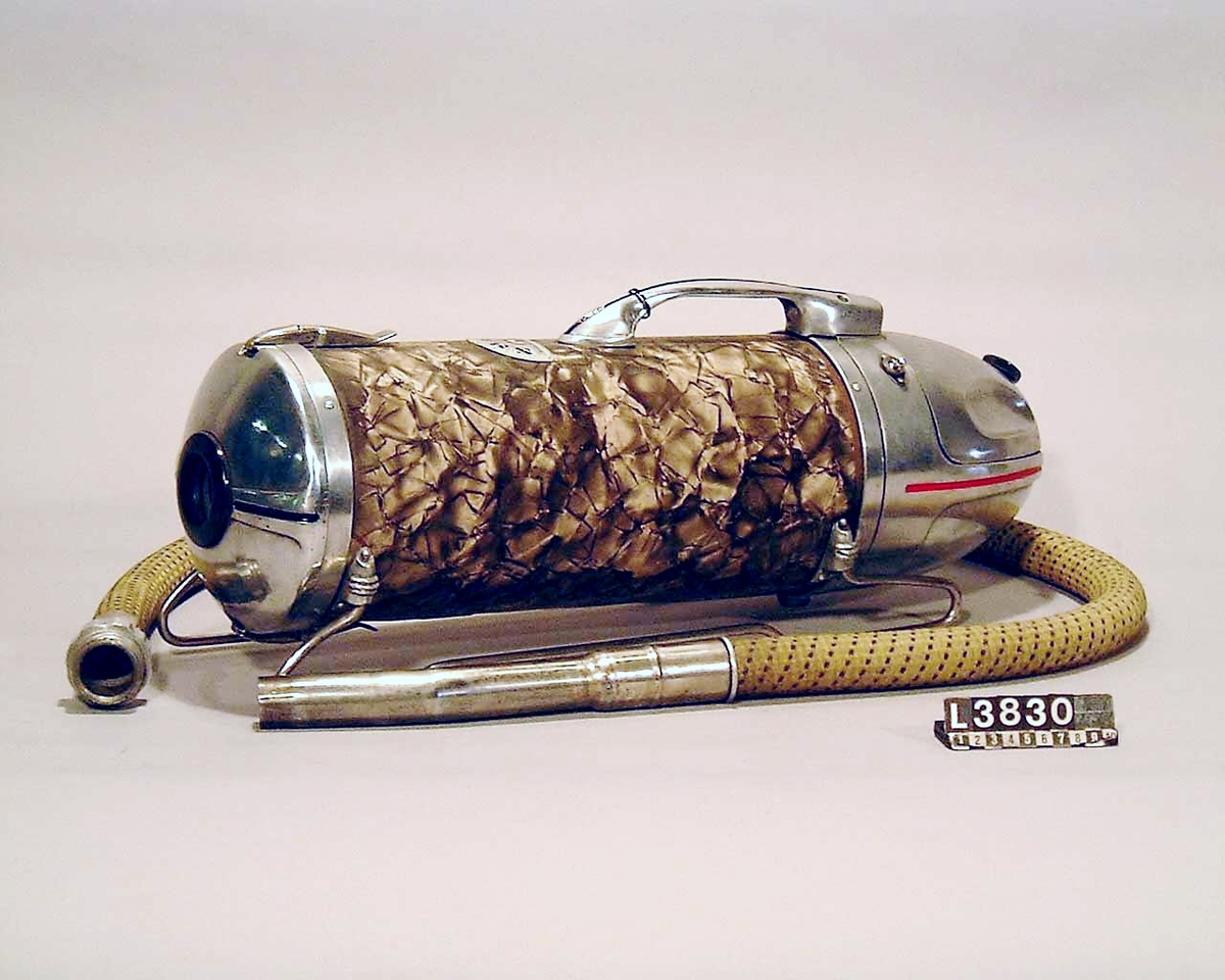 Cylinderdammsugare, klädd i guldaktig skimrande pegamoid. Fram och bakstycke samt medar i blank metall. Apparaten ligger i en koffert/väska. Under apparaten finns en etikett med Nr 30. Alla tillbehör finns, dock ej kabel. De kromade skarvrören är rostangripna.