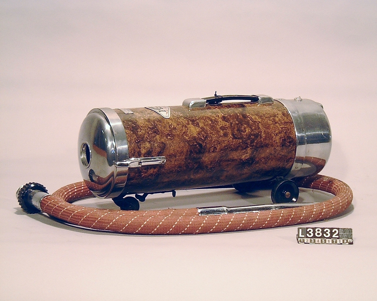 Cylinderdammsugare i brunspräcklig  pegamoid. Fram och bakstycke är i blank metall. Apparaten ligger i en koffert/väska . Under apparaten finns en etikett med Nr 32. Kabel, slang, rör och munstycken  finns.