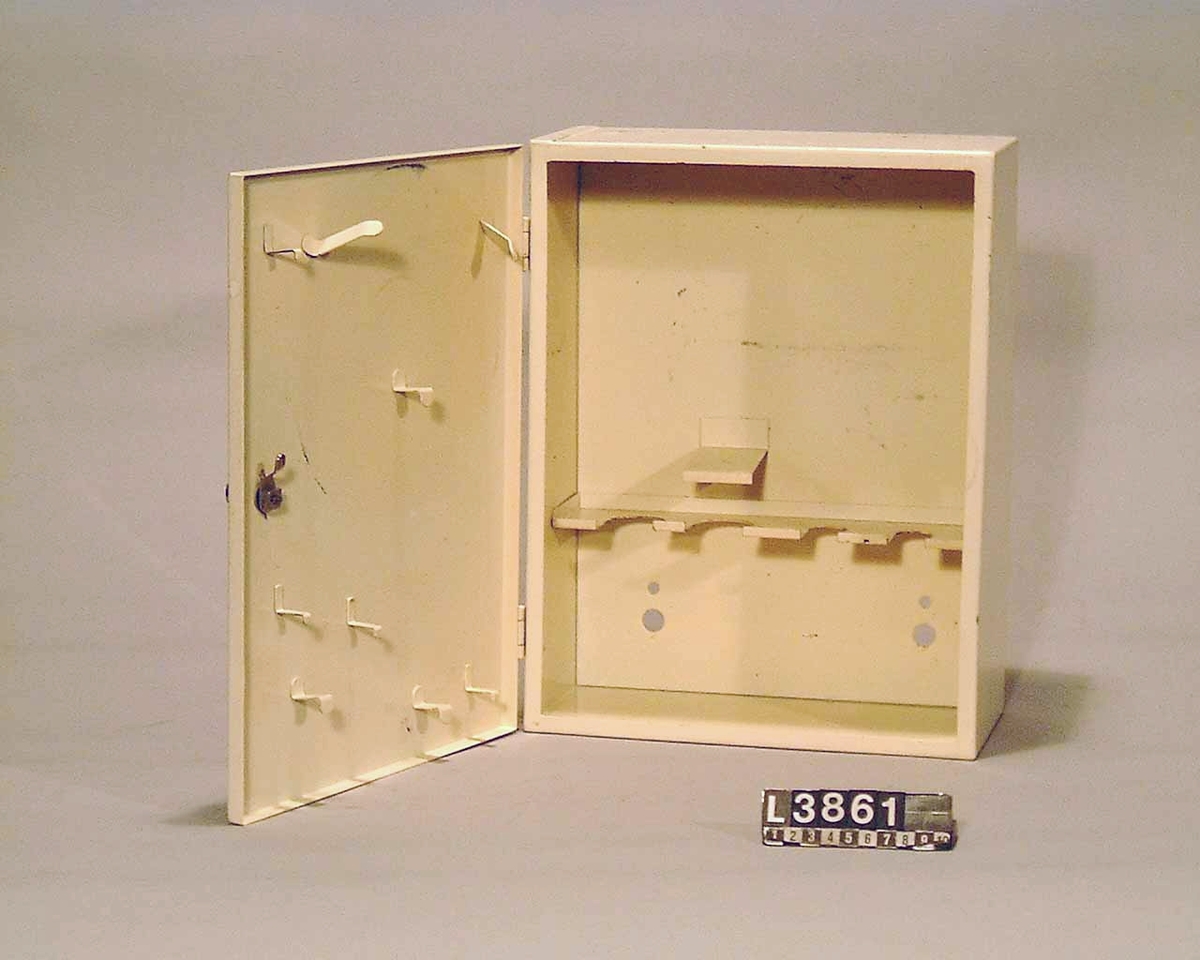 Tillbehörsskåp för Assistenten. Skåpet har ett vridbart lås. Inuti skåpet finns krokar och fästen för att hänga upp de olika delarna. För innehåll, se L3860.