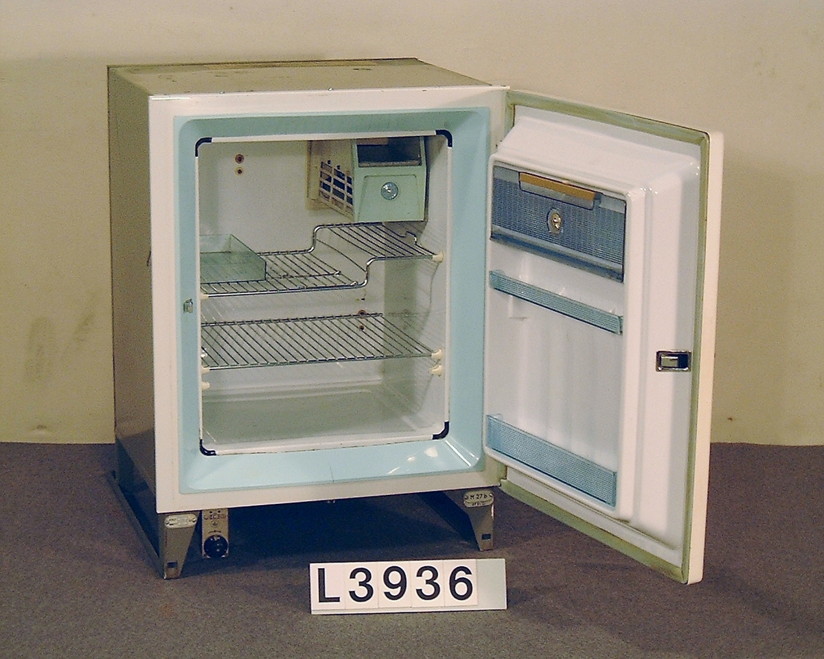 Värmedrivet inbyggnadskylskåp. Fronluckan är benvit och har det klassiska tryckknappshandtaget. Övre och undre ventilgaller saknas.