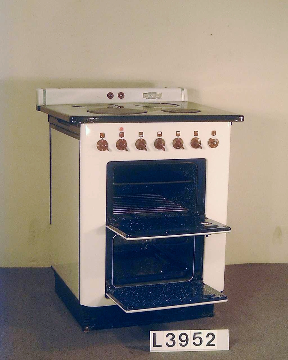 Elektrisk spis med emaljerad front i benvitt. Överhällen är emaljerad i svart. Spisen har ugn och värmeskåp. Strömställarna är i röd plast. Bak på överhällen sitter en panel med signallampor.